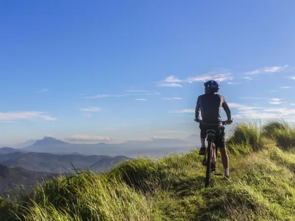 Ciclista en la cima de una colina, disfrutando de las vistas de Galicia en bici. El cielo azul y las montañas de fondo crean un paisaje impresionante.