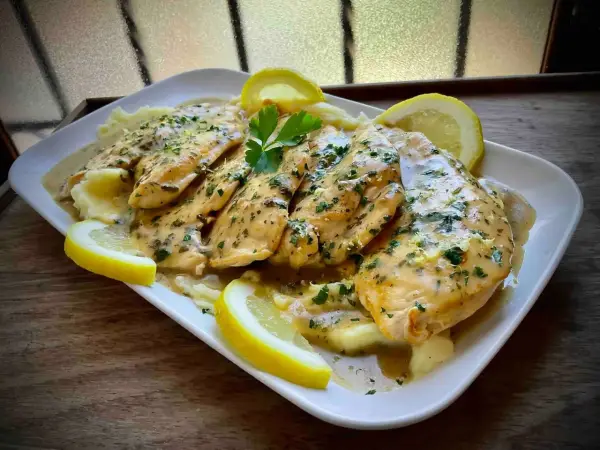 Delicioso pollo al limón con puré de patatas, adornado con rodajas de limón y perejil fresco.
