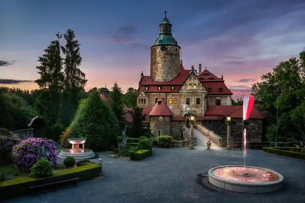 Zamek Czocha o zmierzchu, z fontannami i kwitnącymi rododendronami. Odkryj atrakcje w okolicy tego malowniczego miejsca.