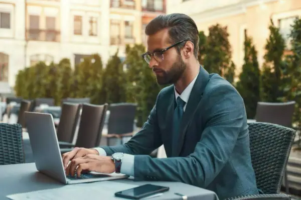 Mężczyzna w garniturze pracuje na laptopie w kawiarni. Jego kod zawodu to prawdopodobnie coś związanego z biznesem.