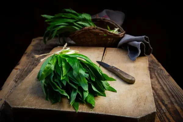 Un bouquet d'ail des ours fraîchement cueilli, prêt pour une recette. Un couteau repose sur la planche à découper en bois.