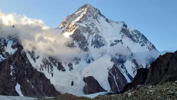Majestatyczny K2, najwyższy szczyt Karakorum, wyłania się z chmur. Słońce oświetla jego śnieżne zbocza, ukazując surowe piękno gór.