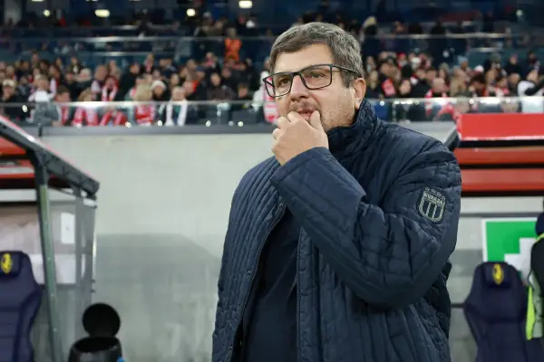 Włoski trener w okularach, zamyślony, w granatowej kurtce z naszywką "ITALIA", stoi na tle trybun stadionu.