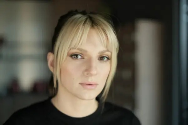 Portret młodej kobiety z blond grzywką i ciemnymi pasemkami włosów, patrzącej w obiektyw.