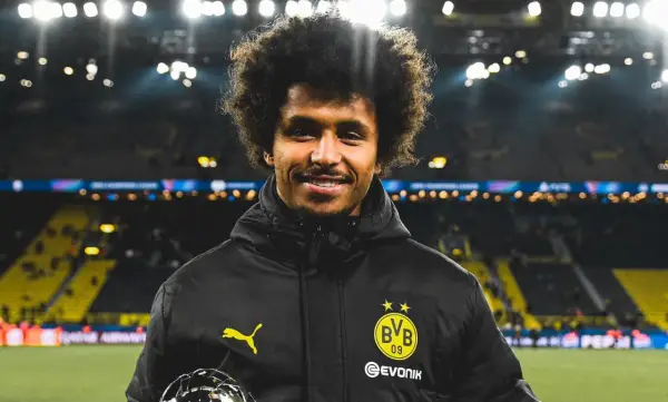 Karim Adeyemi z BVB z pucharem, uśmiecha się na tle stadionu.