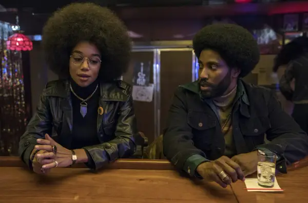 En kvinna med stor afro och en man med skägg sitter vid en bardisk. De är medlemmar i rollistan i Blackkklansman.