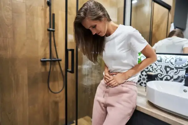 Kobieta w łazience trzyma się za brzuch, zaniepokojona. Czy to plamienie implantacyjne? Zdjęcia mogą pomóc w rozpoznaniu.
