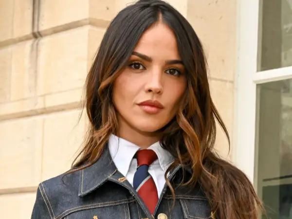 Mujer con cabello castaño y mechas woodlights, viste camisa blanca, corbata y chaqueta vaquera.