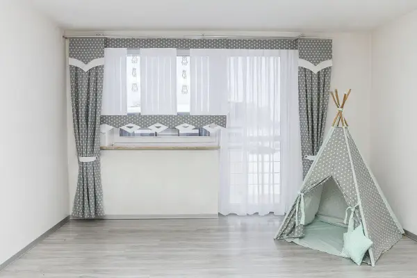 Szare zasłony w gwiazdki i białe firanki idealnie pasują na okno do pokoju młodzieżowego. Obok namiot tipi.