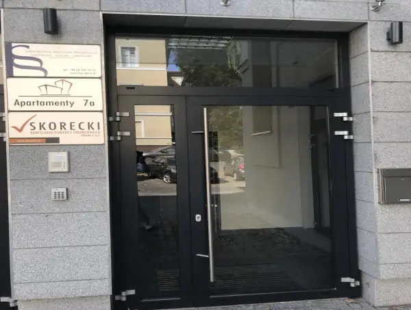 Wejście do budynku z tabliczkami informacyjnymi, w tym "SKORECKI KANCELARIA DORADCY FINANSOWEGO".
