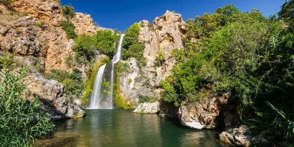 El Salto de Chella, una cascada imponente rodeada de rocas y vegetación exuberante, cae en una poza de agua verde.