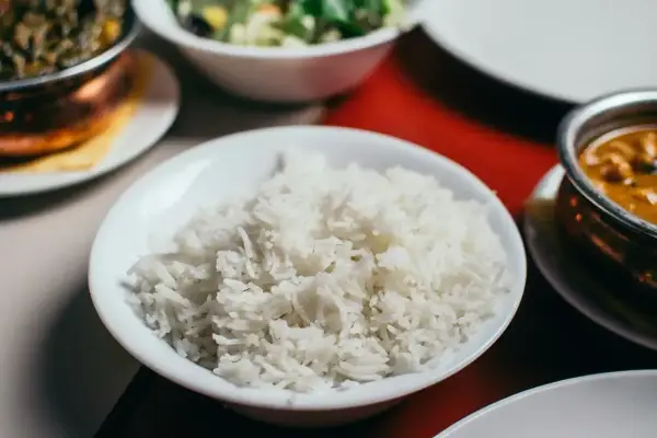 Biały ryż, źródło węglowodanów, w misce obok indyjskiego curry i sałatki.