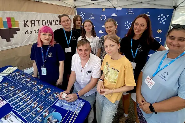 Grupa osób, w tym młodzież i dorosłych, stoi za stołem z książkami i materiałami promocyjnymi "Szkoła w Chmurze".