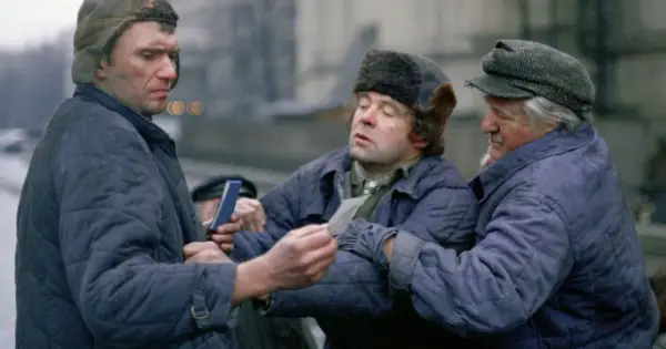 Trzech mężczyzn w zimowych kurtkach i czapkach, w tym jedna z futrzanymi uszami, dyskutuje, trzymając w rękach dokumenty. Scena z filmu "Miś" z niezapomnianą obsadą.