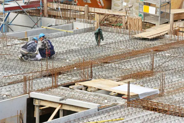 Bauarbeiter prüfen Pläne für verschiedene betondecken arten. Stahlbewehrung für eine massive Betonplatte ist sichtbar.