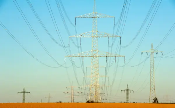 Linie energetyczne na tle błękitnego nieba. Wiele słupów wysokiego napięcia, tworzących sieć, jakby ilustrowało przelicznik MW na KW.
