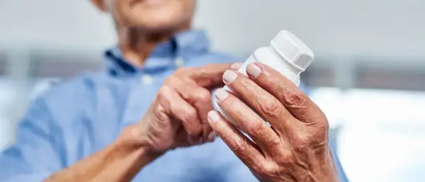 Ältere Hände halten eine Pillendose. Die Glucosamin Wirkung für Gelenke wird hier thematisiert.