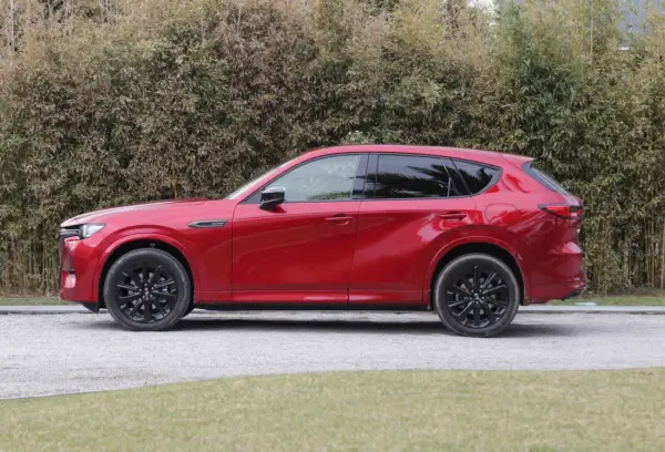 Czerwona Mazda CX-60 3.3 diesel z czarnymi felgami stoi na żwirowej drodze, za nią gęsty żywopłot.