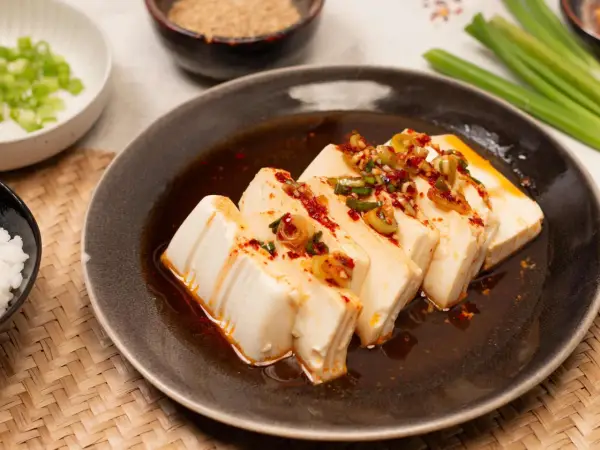 Seidiger Tofu, ein einfaches silken tofu recipe, serviert mit Frühlingszwiebeln und Chili-Öl auf einem dunklen Teller.