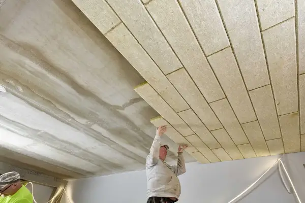 Pracownicy montują płyty izolacyjne, wykonując ocieplenie stropu betonowego.