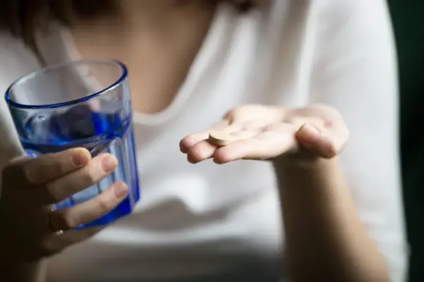 Une main tient un comprimé, peut-être un supplément de sels minéraux, à côté d'un verre d'eau bleue.