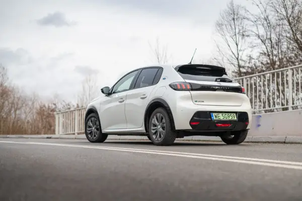 Biały Peugeot e-208 z zieloną tablicą rejestracyjną WE 5G959 zaparkowany na drodze.