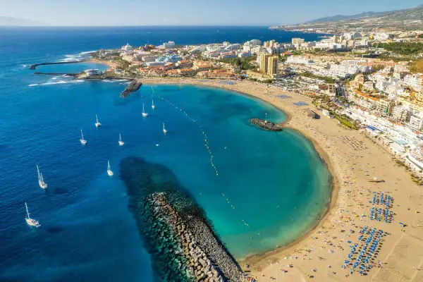 Vista aérea de una bahía con aguas turquesas, veleros y una playa repleta de gente, un ejemplo de las mejores playas Tenerife.