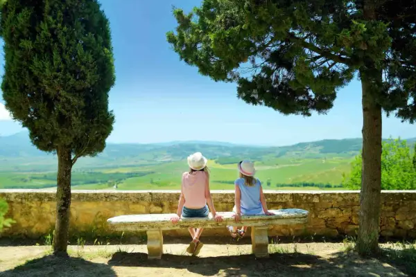 Due bambine con cappello ammirano il panorama collinare toscano, un perfetto weekend con bambini in Toscana.