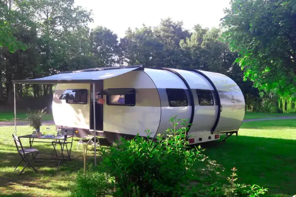 Une caravane XXL extensible, prête pour l'aventure, avec un auvent déployé et une table dressée sur l'herbe.