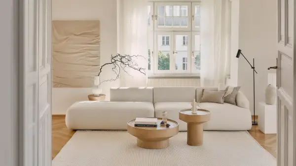 Jasny, przytulny salon z beżowym domem w tle. Miękka sofa, drewniane stoliki i subtelne dekoracje tworzą spokojną atmosferę.