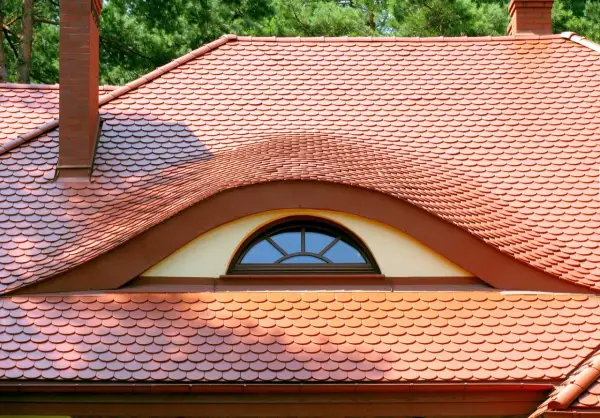 Ceglana dachówka ceramiczna w kształcie rybiej łuski, z ozdobnym lukarną. Idealna, by stworzyć stylowy dach.