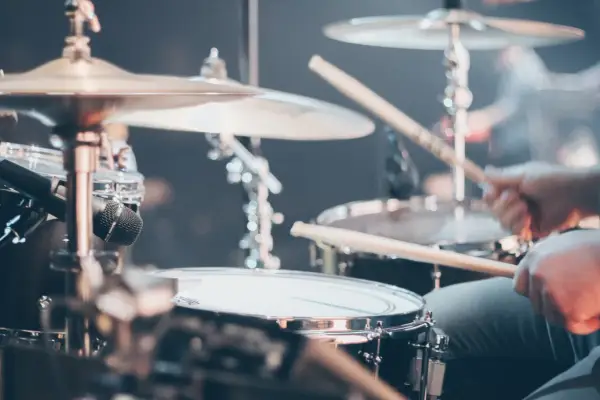 Gros plan sur un set de batterie, avec des baguettes en action. Différents types de tambour et cymbales sont visibles.