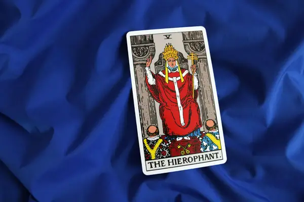 Karta Tarota "The Hierophant" na niebieskim tle. Postać w czerwonych szatach z tiarą i krzyżem.
