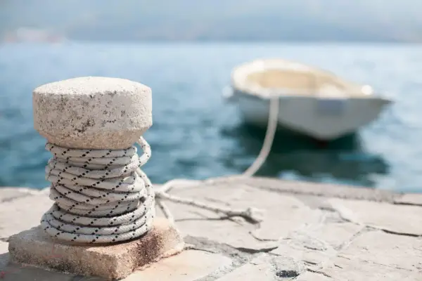 Un cordage est enroulé autour d'une borne en pierre sur un quai, prêt pour le prochain pendille bateau.