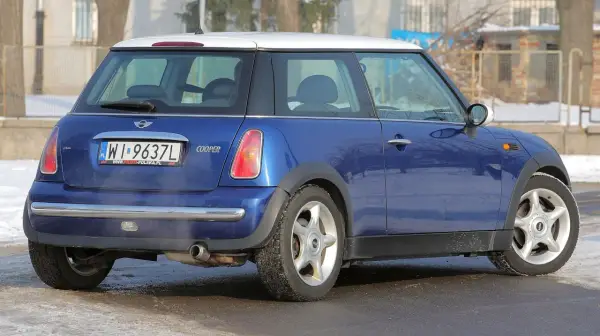 Niebieski Mini Cooper R50 z białym dachem, zaparkowany na zaśnieżonej drodze.