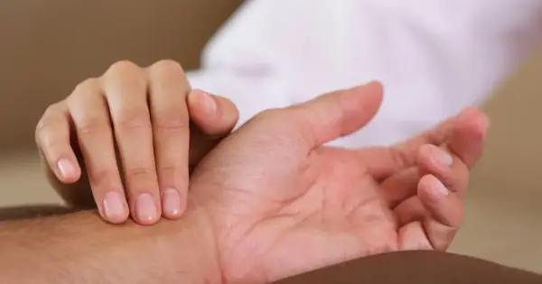 Dłoń pielęgniarki bada tętno na nadgarstku pacjenta, sprawdzając prawidłowe tętno.