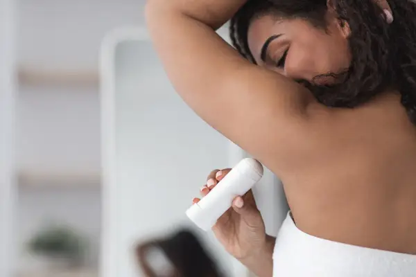 Kobieta aplikuje biały antyperspirant pod pachę, pokazując, jak działa antyperspirant, by czuć się świeżo przez cały dzień.