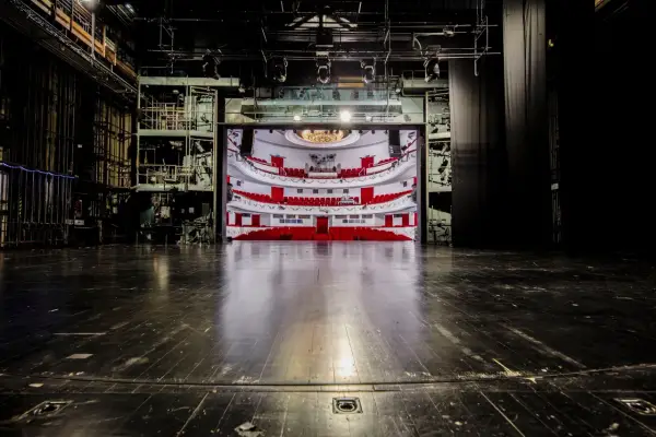 Widok na pustą widownię z czerwonymi fotelami i balkonami, widziany ze sceny. To wnętrze teatru dramatycznego w Warszawie, gotowe na spektakl.