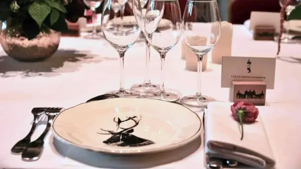 Élégante disposition des couverts à la française sur une table dressée, avec une assiette décorée d'un cerf, des verres à vin et une carte de visite.