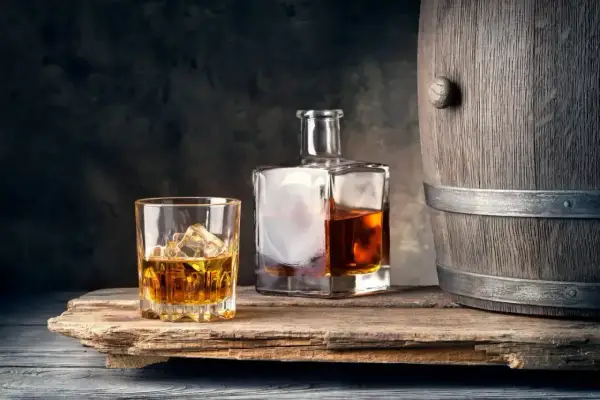 Szklanka z lodem i butelka whisky obok drewnianej beczki. Idealne połączenie, by dowiedzieć się, z czym pić whisky.