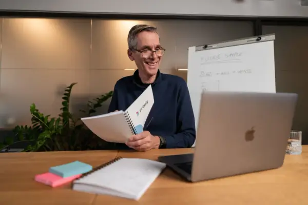 Lehrer erklärt **adjektive und adverbien englisch** mit einem Flipchart und Notizbuch.