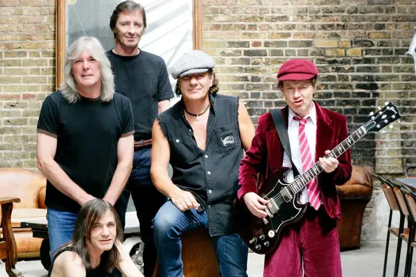 Zespół AC/DC w komplecie, gotowy do rock and rolla. Angus Young z gitarą, Brian Johnson w kultowym stroju.