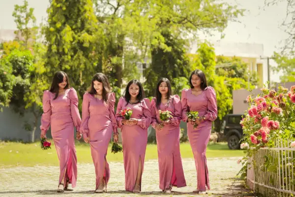 Cinq demoiselles d'honneur en robes roses marchent ensemble, tenant des bouquets.