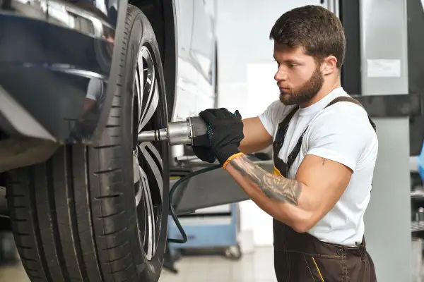 Mechanik z tatuażem dokręca śrubę koła. Zwróć uwagę na objawy zużycia sworznia wahacza, gdy słyszysz stuki.