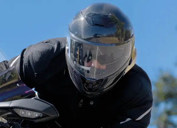 Motociclista con un casco mas silencioso de fibra de carbono, disfrutando del paisaje en un día soleado.