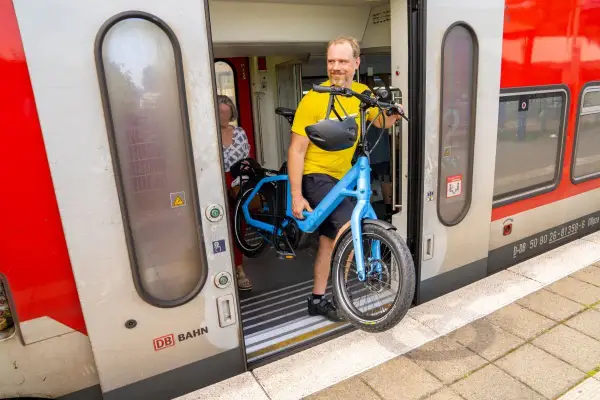Mann mit blauem E-Bike steigt in den Zug. Perfekt, um das E-Bike im Zug mitzunehmen und die Reise fortzusetzen.