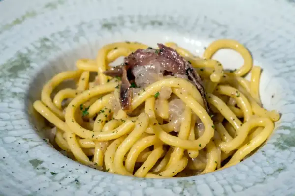 Un piatto di spaghetti con acciughe e prezzemolo, un'ottima idea per scoprire cosa mangiare a Padova.