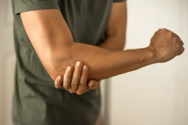 Person håller om sin armbåge, som om den har ett avslitet ledband.