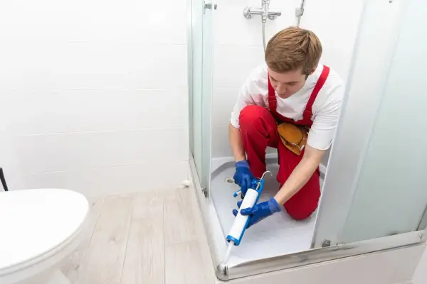 Installatore usa silicone per box doccia, sigillando la base per prevenire perdite d'acqua.