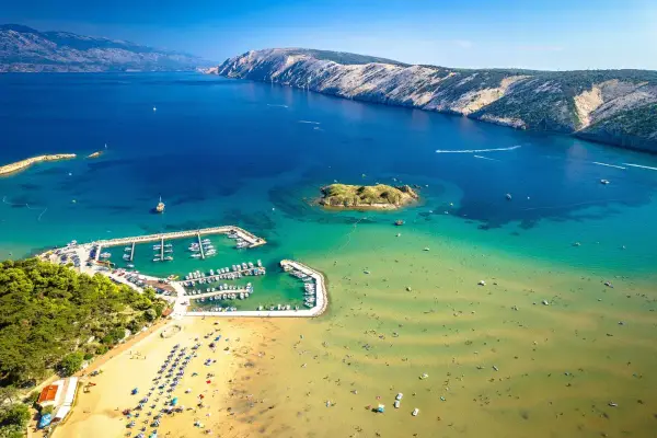 Piaszczyste plaże w Chorwacji, z turkusową wodą, łodziami w marinie i ludźmi cieszącymi się słońcem.